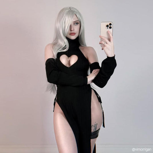 Person wearing a black outfit with a high slit, taking a selfie against a plain background.