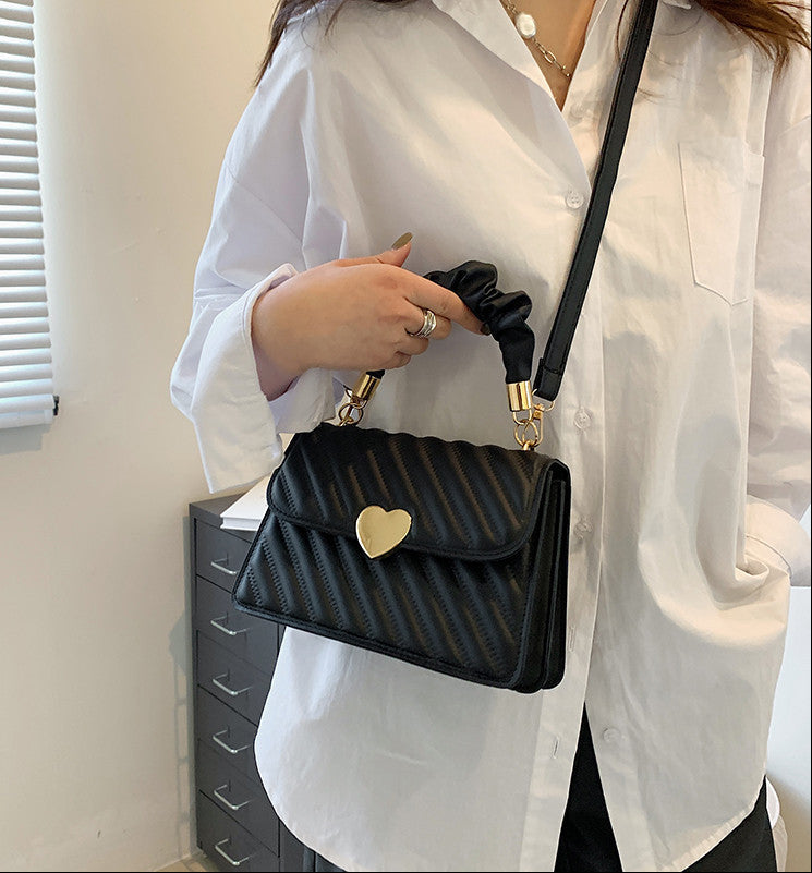 Person holding a black handbag with a gold heart emblem, wearing a white shirt. Quilted Chain Shoulder Bag – Small Square PU Crossbody with Love Metal Design Handbags mpncm1-10.myshopify.com quilted-chain-shoulder-bag-love-metal-crossbody-pu Fittyluxe