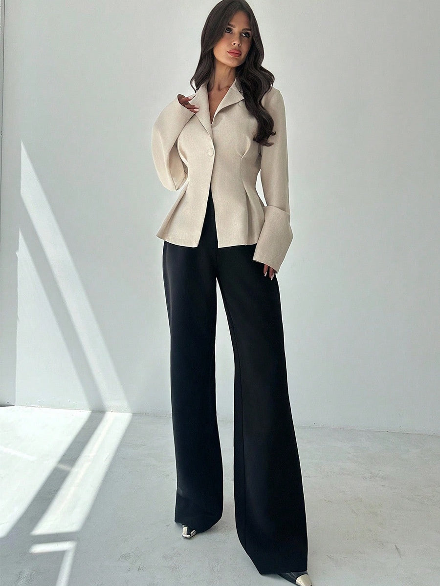 Woman wearing a beige jacket and black pants in a minimalistic setting